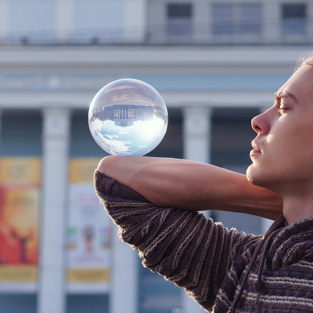 Guy balances with glass ball on bent elbow; Inverted panorama of city in reflection of ball