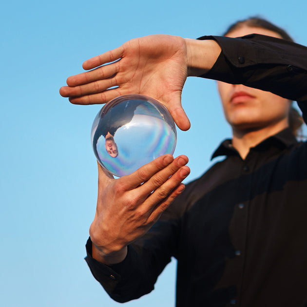 Guy balances with glass ball; Inverted panorama of sky in reflection of ball