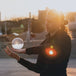 Guy balances with glass ball on hand; Inverted panorama of city in reflection of ball. 