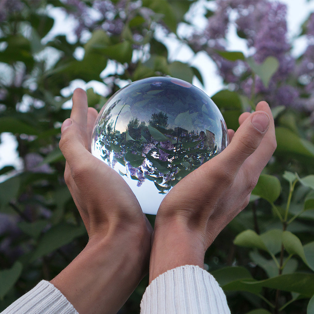 Hands holding contact juggling ball; The flowering lilac bush is reflected in the glass sphere