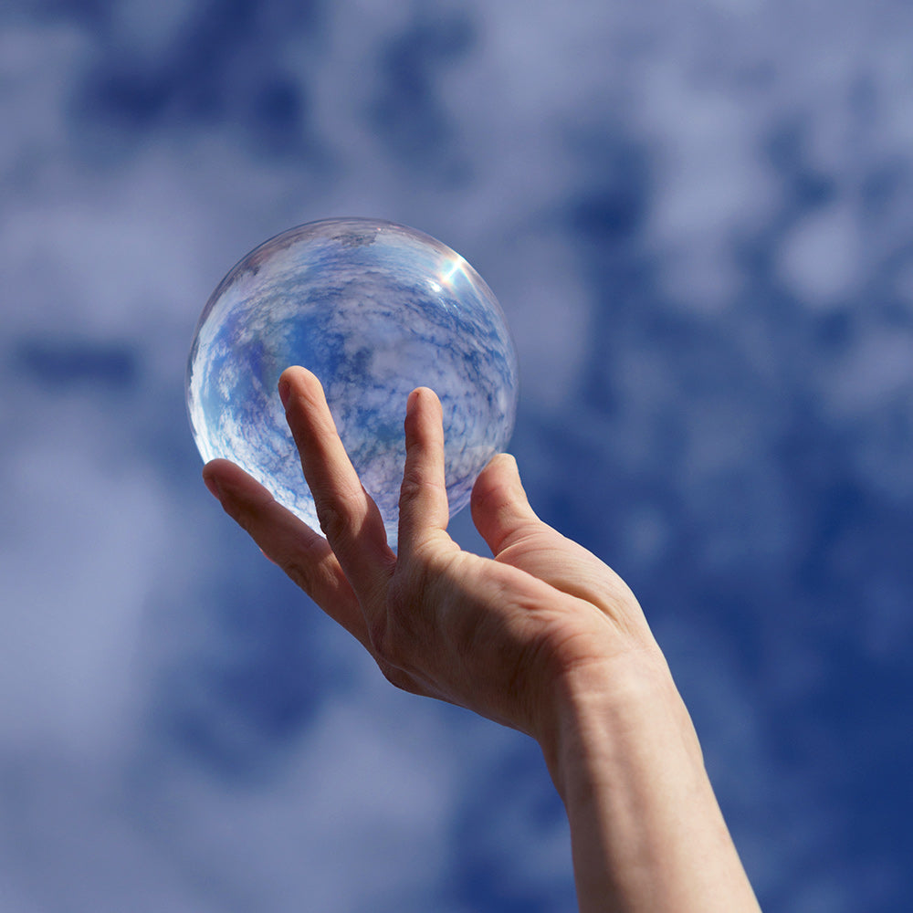 Close-up of hand holding 90mm Clear Contact Juggling Ball in sky background; Inverted panorama of sky in reflection of ball